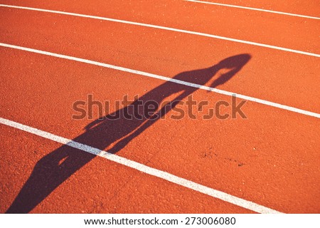 Young woman shadow on a stadium running path. Diagonal angle view. Sport concept