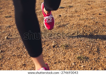 Young woman in red training shoes running off road on a sunset. Close-up dynamic photo