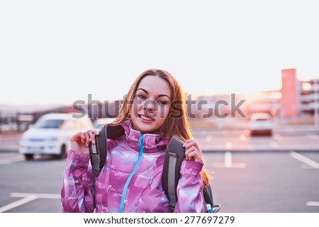 Attractive young woman looking to camera while adjusting her backpack. A bit tired but still ready to continue her trip. Freedom, tourism and backpacking concept. Urban scenery