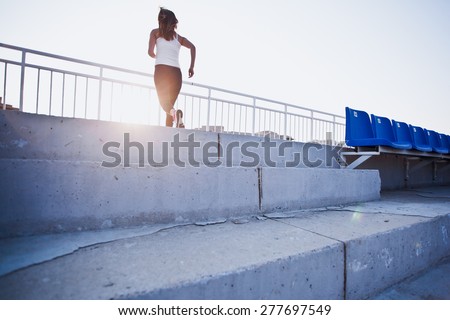 Young woman running to a sunlight on a stairs of a stadium between stands. Sports, motivation and running concept. Conceptual photo. Copy space
