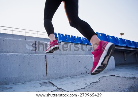 Sporty woman legs with sneakers running upstairs of a stadium between stands. Sports, motivation and running concept. Conceptual photo. Copy space. Concrete steps
