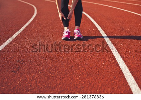 Woman hands massage her leg calf preparing for run front view. Sporty girl feet on a race track on stadium. Brightly lit scene. Copy space