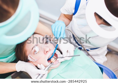 Woman dentist and her assistant at medical procedure. Check-up for patient healthy teeth with dental braces. Medical instruments in doctor hands. Bracket cleaning. Teeth reflection in a mirror