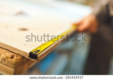 Worker measures wooden deck with tape measure in workshop. Selective focus photo