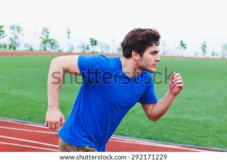 Attractive man runner in blue shirt running fast in front of football field. Success, power and speed concept