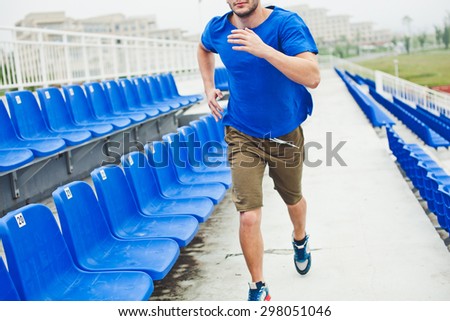 Man runner in blue shirt and shorts running between stands on stadium unrecognizable photo cropped by neck no face. Technique of running