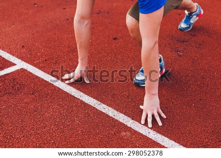 Man runner in blue shirt and shorts and sport shoes in steady position before run at start of race track preparing for run on a stadium unrecognizable no face focus on hands