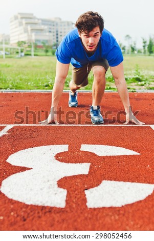 Man runner in blue shirt and shorts and sport shoes in steady position before run at start of race track preparing for run on a stadium with huge white lane number 3