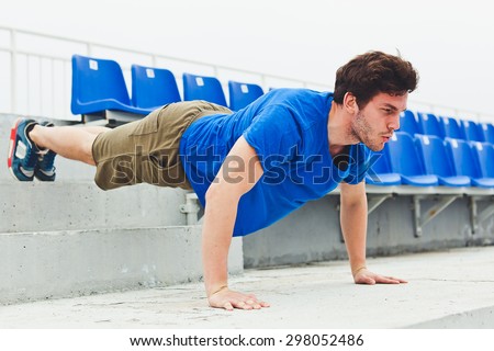 Young sporty handsome man training on a stadium stairs during hard workout performing push-ups in stressed position up
