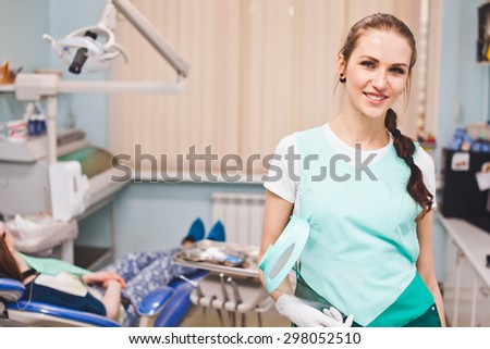 Young beautiful woman dentist smile cheerfully when handing full face protection shield standing in her office in front of dental chair with patient. Copy space