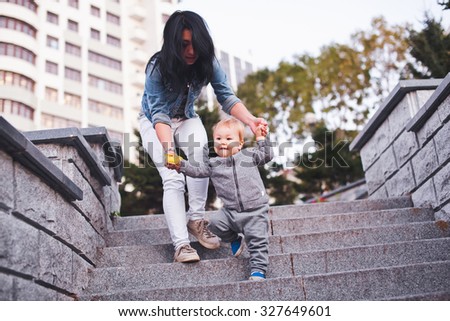 Beauty young asian woman mom with freckles and her son relaxing outdoors. Mother with dark hair and her son is blond. Unusual appearance and heredity concept. Mom helping her son go down the ladder