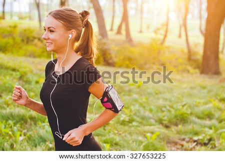Young attractive female runner with armband running on sunset in park with earphones listening to music during training. Copy space