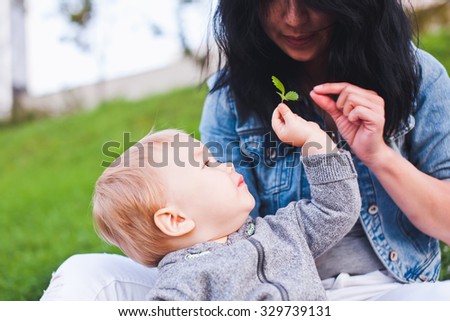 Baby boy gives his young mother a green leaf sprout tree in future. Boy is blond haired mixed race, mother is brunette asian. Concept of nature, family and sharing. Copy space