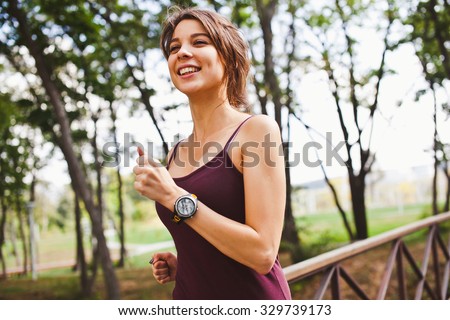 Young attractive sporty smiling woman running in forest wearing sport gadget pulse meter running tracker on wrist side view with copy space