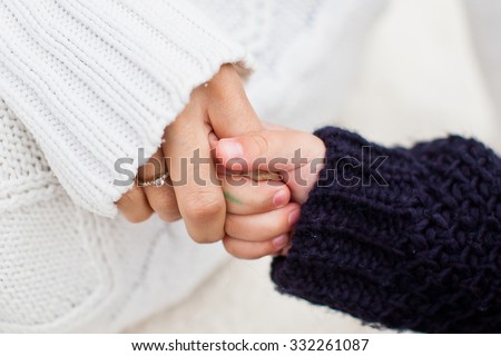 Mother holding her daughter hand. Daughter holding mom\'s finger. Both in warm and cozy sweaters. Daughter in blue sweater and mother in white sweater. Conceptual photo of diversity and family