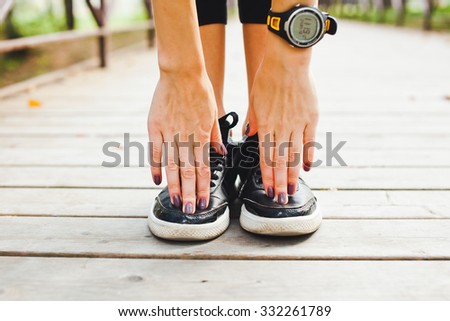 Athletic fit girl stretching in park in summer after training workout before run. Smart watch pulse meter on hand. Touching toes to stretch well. Front view central orientation