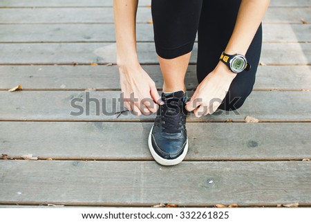 Young girl athlete tying up her laces with smart watch pulse meter cardio monitor on wrist during training at sunny day in park on a boardwalk on wooden background. Unrecognizable. No face. Copy space