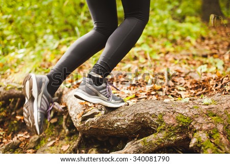 Young woman in sportswear and sports shoes running in forest at fall path with leaves on ground. Legs view running along tree roots in park