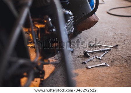 Row of screws and wrench tools on a floor in workshop near repaired old bike or motorcycle engine. Industrial scene with equipment on background and blurred foreground