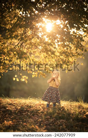 Adorable toddler girl eating an apple in the park. Autumn. Colorful leaves. Magic back light. Sunset