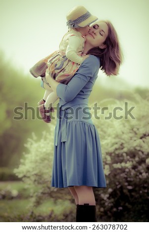 Adorable toddler girl kissing her Mom in the park. Special colors.