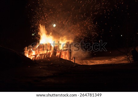 Big fire at night. Wood house ruins. Dark night. Light sparkles flying around the trees