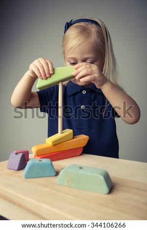 Adorable toddler girl playing with wood construction set. Serious, curious face. Inquiring mind