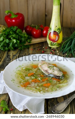 Homemade soup of fish and pearl barley on a wooden table