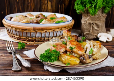 Baked chicken drumsticks with potatoes, mushrooms and cauliflower served on a wooden table. Rustic style