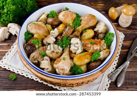 Baked chicken drumsticks with potatoes, mushrooms and cauliflower served on a wooden table. Rustic style