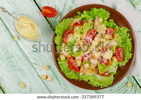 Caesar salad with chicken, croutons and greens on wooden table