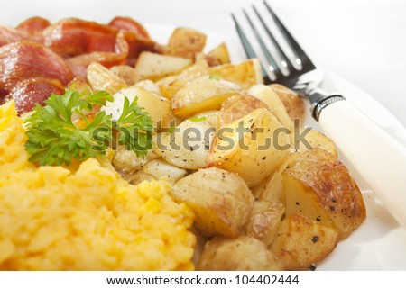 Breakfast of home fries or saute potatoes, with grilled bacon and scrambled egg.