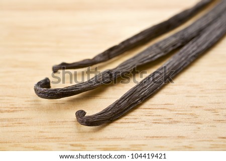 Close up shot of three vanilla beans on a wooden board, shallow DOF.