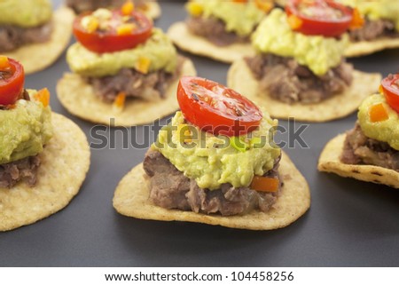Spicy Mexican party food, corn chips topped with refried beans, avocado and tomato salsa.