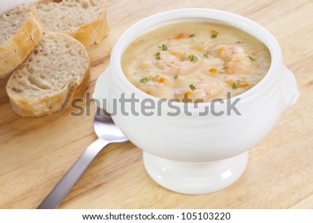 Fish chowder with prawns in a lions head bowl, with bread, on a pine board.