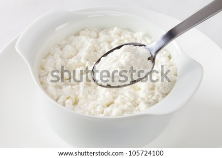 A bowl of cottage cheese, and a spoon lifting out a spoonful.