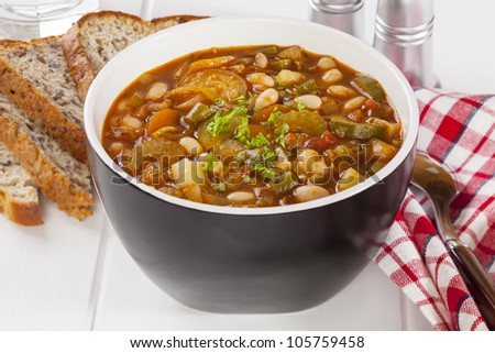 A bowl of vegetable soup on a table with bread.