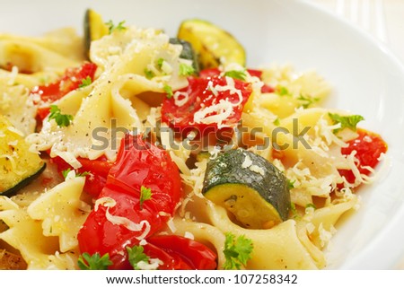 A bowl of pasta bows or farfalle with roast courgettes or zucchini, red pepper and tomato with olive oil and herbs.