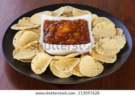 A bowl of mango chutney, set on a plate and surrounded by mini poppadums.