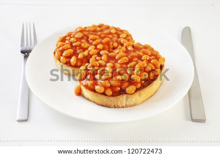 Baked beans on thick sliced white toast with knife and fork. An easy,nourishing meal.