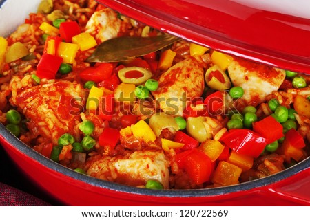 Chicken and rice dish, arroz con pollo, from Latin America, with chicken, rice, beer, tomatoes, capsicums, peas, paprika, cumin, oregano, in a red cast iron casserole.