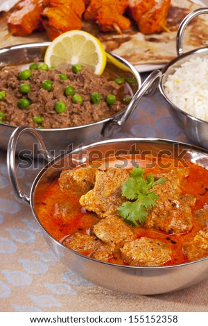 A selection of Indian foods, with lamb rogan josh, keema matar, chicken tikka, naan bread and basmati rice. Focus on lamb.