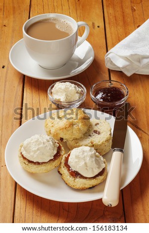 Devon cream tea, scones, jam, cream and a cup of tea, on an old pine table.
