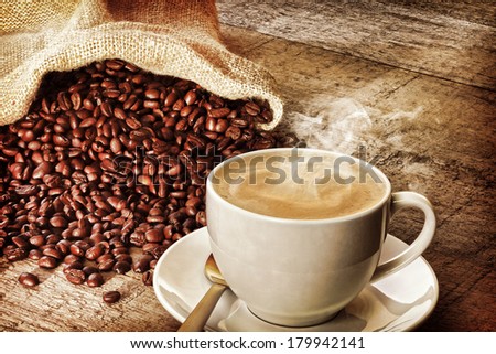 Coffee and Sack of Coffee Beans - a cup of hot steaming espresso coffee on a rustic plank background, with a sack of coffee beans. Front to back focus. Instagram effect.