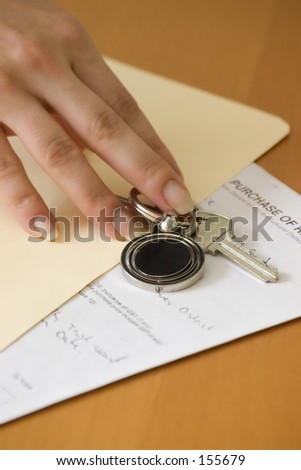 Fingers reaching for a set of keys which are on top of a manilla folder, with a contract inside,
