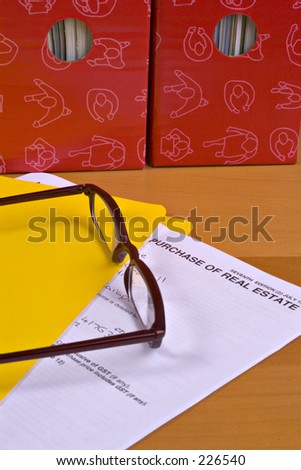 Spectacles on real estate contract,yellow folder, red magazine files behind