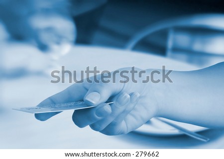 Blue tone hand offering credit card, background is blurry cafe.