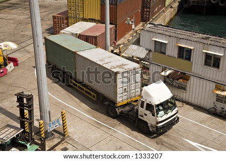Stock photo of shipping containers on semi-trailer leaving a container terminal on Victoria Harbour Hong Kong, stacked containers in background.