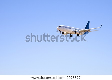 Boeing 737 in completely clear blue sky, with undercarriage and flaps down and landing lights on, as it makes its final approach before landing.