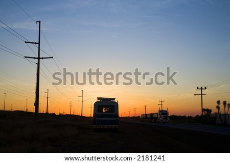 Twilight in an industrial area, and a road train is passing a bus on opposite sides of road, power lines on both sides, lots of copy space.